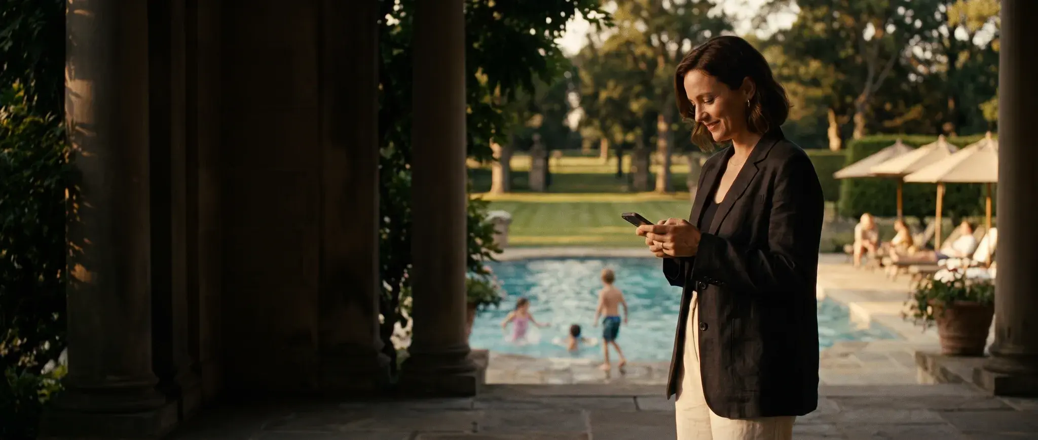 A member on the club terrace by the pool, her children swimming behind her